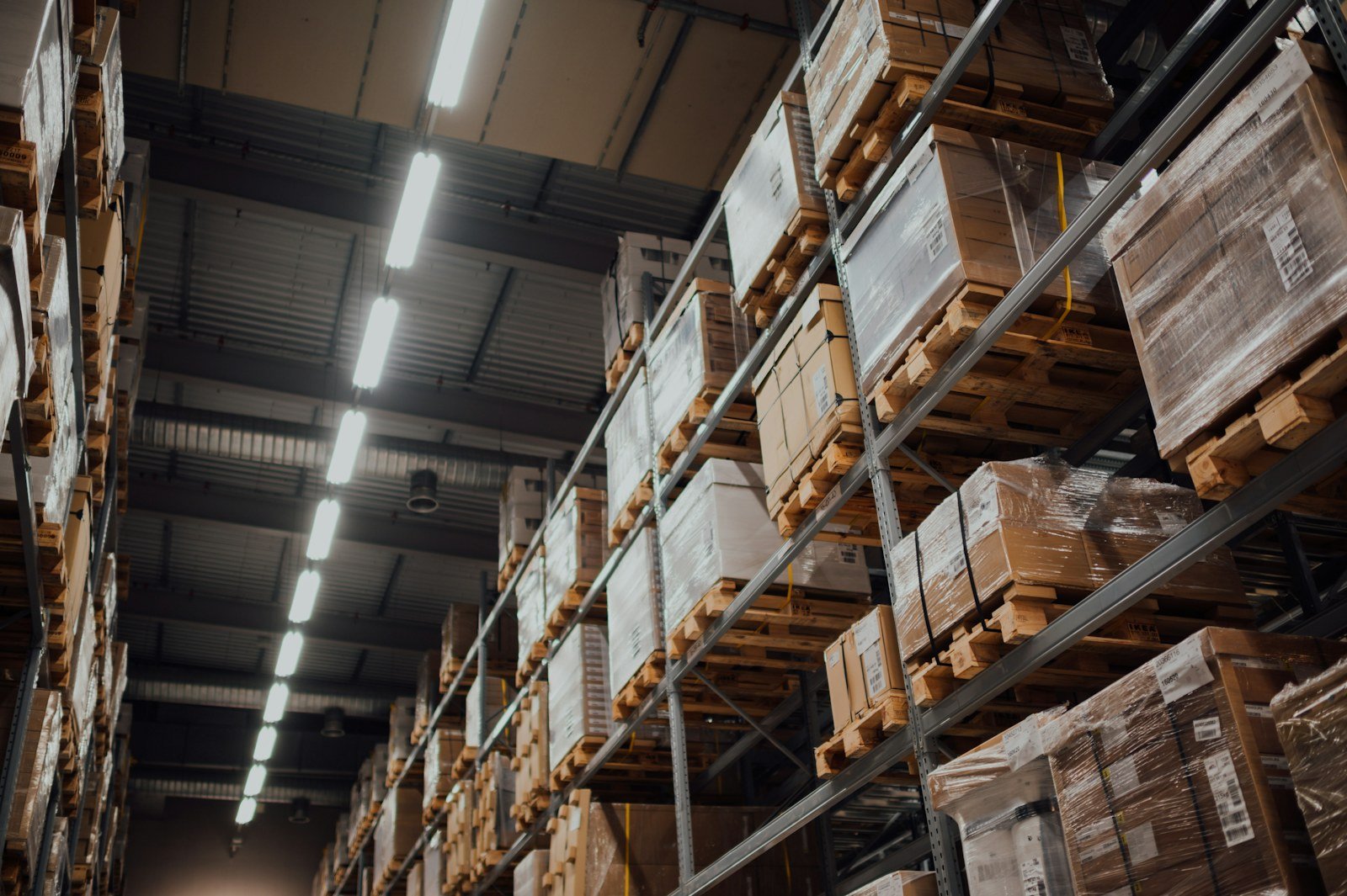 Warehouse racking stacked with palletized boxes under long overhead lights