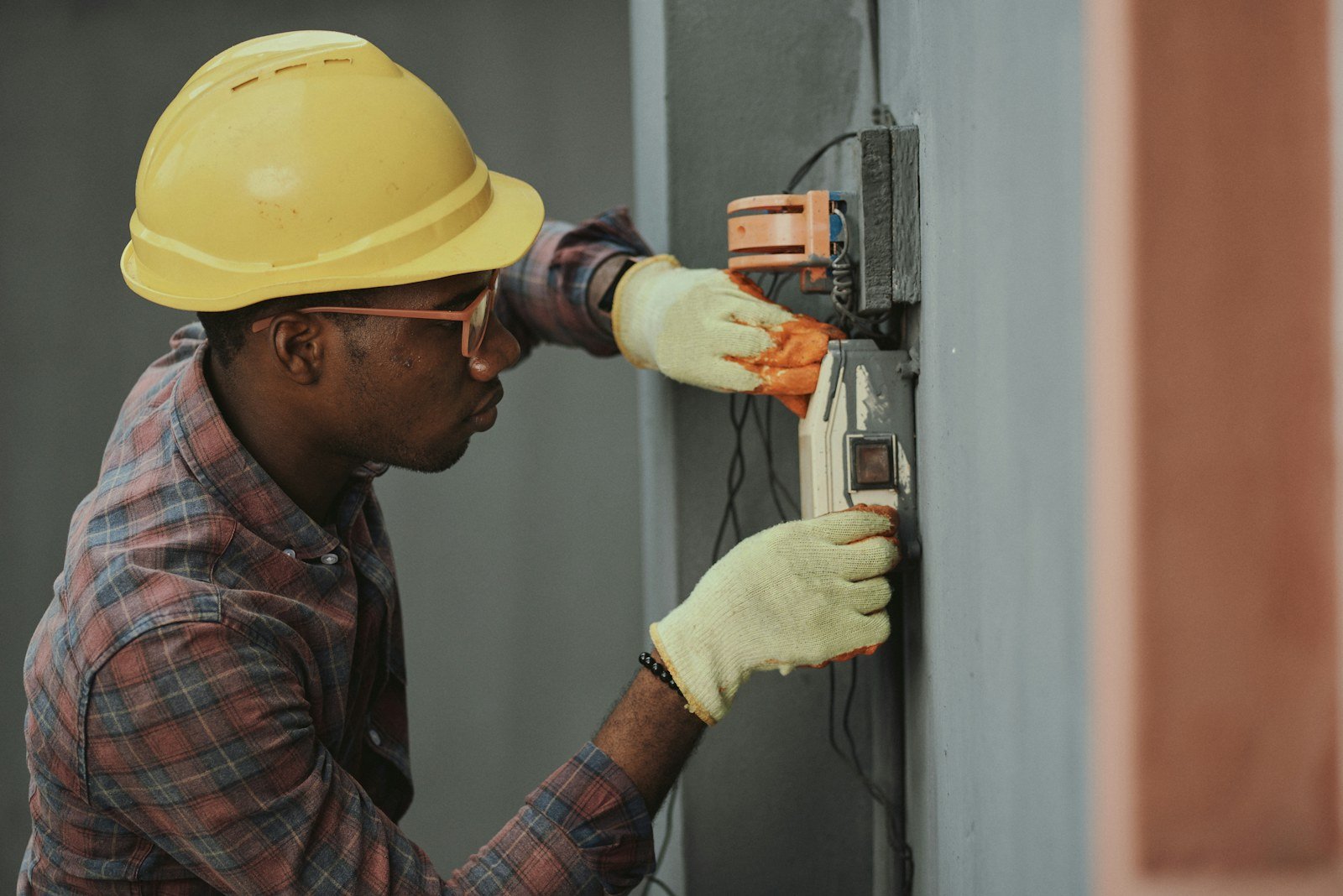 An electrician in a hard hat and work gloves connecting wiring on a site visit