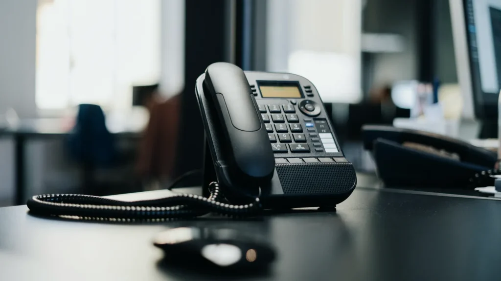 Black office desk phone with a coiled cord on a dark desk
