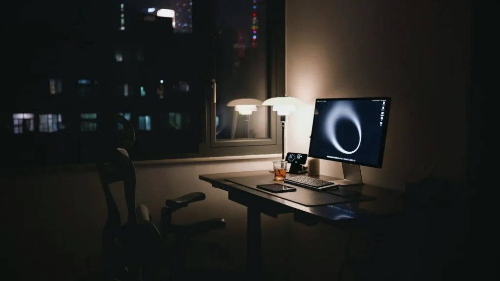 Dark home office at night with a desk lamp and a glowing monitor on the desk